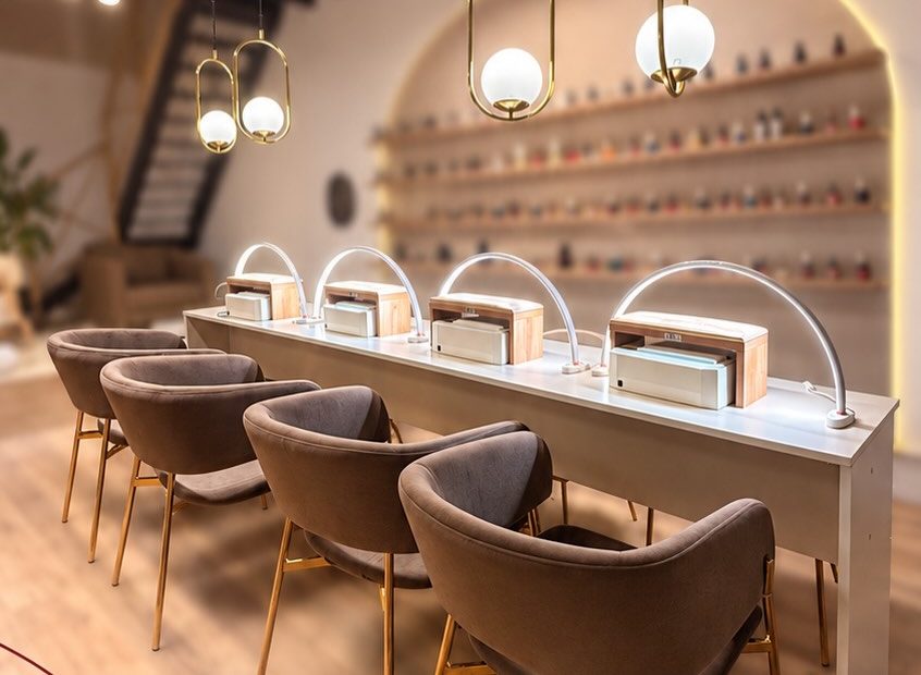 Sector de uñas de Oi Spa: mesada con lámparas, sillones marrones y estante con esmaltes en un nicho en arco
